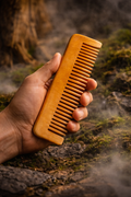 Hand holding a wooden comb against a natural background. Anti-frizz wooden comb with smooth wide teeth for hair growth and scalp care